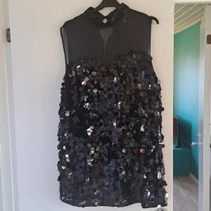 Svart paljettklänning med pärlkrage - Supersnygg svart kortklänning täckt av stora paljetter och med en cool pärlbeströdd krage. Klänningen är ärmlös och har en lätt transparent ovandel som ger en extra edge. Bara använda en gång.