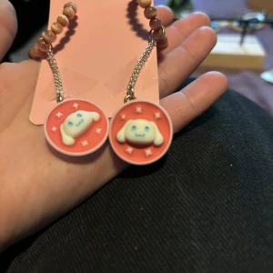 Söta örhängen med hundmotiv - Supergulliga örhängen med runda hängen i rosa och vitt, dekorerade med en söt hund med blå ögon och öron. Örhängena har kedja och pärlformade detaljer i beige. Perfekta för dig som gillar kawaii-stil och vill sticka ut lite extra.