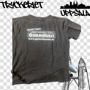 Svart t-shirt Svenska Gummihuset - Svart t-shirt med vit tryckt logga och text på ryggen från Svenska Gummihuset. Klassisk passform med korta ärmar och rund hals. Perfekt för dig som gillar streetwear med en touch av reklamstil.