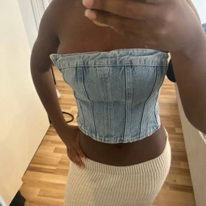 Ljusblå jeans topp från Zara - Snygg ljusblå jeans topp från Zara. Toppen är axelbandslös och croppad med markerade sömmar som ger en cool och trendig look. Perfekt till sommarens outfits och lätt att matcha med både kjol och byxor.