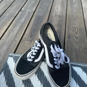 Svarta Vans Old Skool sneakers - Klassiska Vans Old Skool sneakers i svart med vit sula och vit sidosnirk. Skorna har vit snörning, rund tå och är tillverkade i en mix av mocka och canvas. Perfekta för en avslappnad streetstyle-look. Använda men inga synliga anmärknnngar 