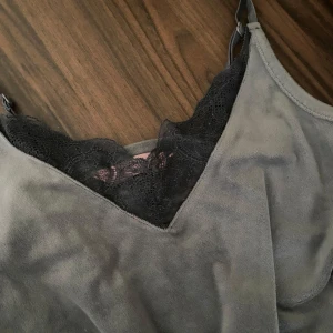 Grå linnetopp med spets från Hunkemöller - Supersnygg grå linnetopp från Hunkemöller i mjukt material med tunna axelband och v-ringning. Toppen har svart spetsdetalj längs urringningen och nertill, vilket ger en extra touch. Perfekt att styla med jeans eller kjol för en chill look.