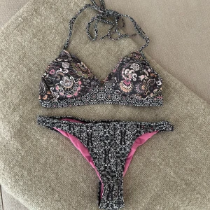 Blommig bikini från Odd Molly - Supersnygg bikini från Odd Molly med blommigt mönster i svart, rosa och vitt. Överdelen har trekantsform med knyt i nacken och byxan har rosa foder. Perfekt för stranden eller poolen, och riktigt unik design! HELT OANVÄND 🌸