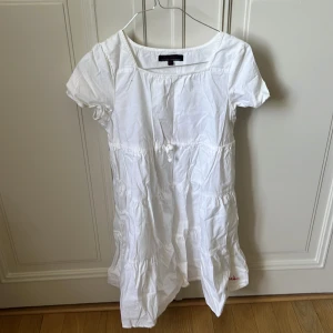 Vit kortklänning från Bondelid - Supersöt vit kortklänning från Bondelid i bomull med korta ärmar och volangdetaljer. På ryggen finns ett broderat rött hjärta och texten 'wherever you go, there you are...'. Perfekt för sommarens alla dagar!