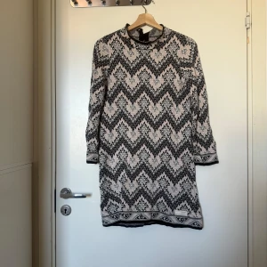 Mönstrad stickad klänning i svart och grått - Snygg stickad kortklänning med svart och grått zigzag-mönster på ljus botten. Klänningen har lång ärm, rund hals och fina detaljer vid ärmslut och nederkant. Perfekt för dig som gillar grafiska mönster och vill ha något bekvämt men ändå stilrent. Från märket Odd Molly i storlek 1 som ungefär motsvarar en storlek S. Mycket fint skick, jag hittar inga synlig anmärkningar eller defekter.  