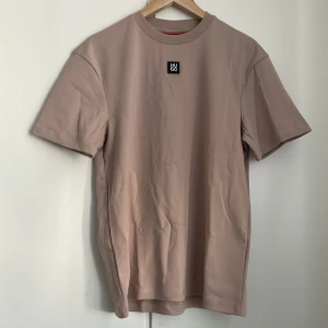 Beige t-shirt från HUGO, storlek XL - Snygg beige t-shirt från HUGO med klassisk passform och diskret logopatch på bröstet. T-shirten är i mjuk bomull och har rund hals och korta ärmar. Perfekt för en clean och stilren look.