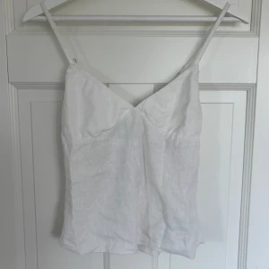 Vit linnetopp från Brandy Melville - Supersöt vit linnetopp från Brandy Melville med smala axelband och v-ringning. Toppen är i luftigt linne och har en avslappnad passform, perfekt för varma dagar. Enkel och stilren design som är lätt att matcha med allt. Den köptes i butik i Barcelona, och finns inte på hemsidan. Den fjärde bilden är väldigt lik i passformen på toppen. Du kan även komma privat om du vill ha bild med den på! 
