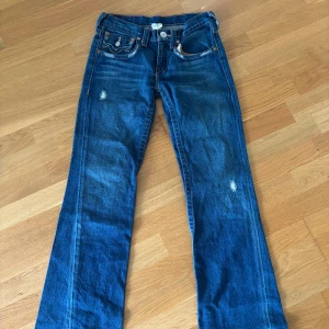 Blå jeansbyxor från True Religion - Säljer ett par klassiska blå jeans från True Religion med kontrastsömmar och broderade bakfickor. Byxorna är bootcut och i bra skick. 