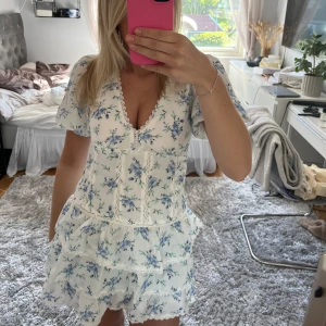 Sommarklänning💛 - Superfin vit kortklänning med blått blommönster och volangdetaljer. Klänningen har v-ringning, korta puffärmar och är figursydd. 
