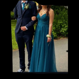 Blågrön glittrig balklänning med spetsdetaljer - Säljer en balklänning i färgen petroleum/blågrön med glittrigt i kjolen och v-ringad överdel med spetsdetaljer. Klänningen har smala axelband och ett flytande, elegant fall. Perfekt för bal eller fest. Har ingen bild på baksidan men den är liknande som framtill men lite mer v-ringad. Använd 1 gång så den är som ny. Den är lite uppsydd framtill nertill. Jag har gett 5400kr för den, men vid snabbare affär så kan jag gå ner lite i pris. 😊🩷🌸