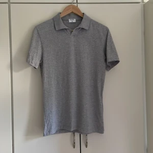 Grå piké t-shirt från Filippa K - Säljer en stilren grå piké t-shirt från Filippa K. T-shirten har klassisk krage och korta ärmar, perfekt för en clean och enkel look. Tillverkad i mjukt material som känns skönt mot huden.