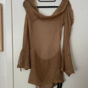 Beige stickad klänning med vida ärmar - Säljer en beige stickad klänning med vida ärmar och snygg, vid halsringning. Klänningen är genombruten och har knytband vid ärmsluten. Perfekt för lager-på-lager eller som strandplagg.