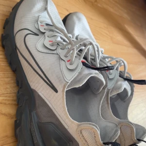 Nike react vision unisex - Nike sneakers i ljusgrått med svarta detaljer och sula. Skorna har snörning, tydlig Nike-logga på sidan och en robust, mönstrad sula som passar för utomhusaktiviteter. Perfekta för dig som gillar sportig stil. Köpt i zalando, har kvitto. Knappt använt så de är nya.