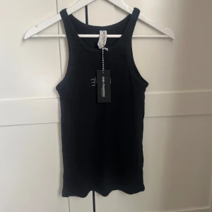 Svart ribbad linnetopp från One Teaspoon - Säljer en svart ribbad linnetopp från One Teaspoon med broderad text 'LOVE' framtill. Toppen har ärmlös design och rund halsringning. Perfekt för en stilren och enkel look.