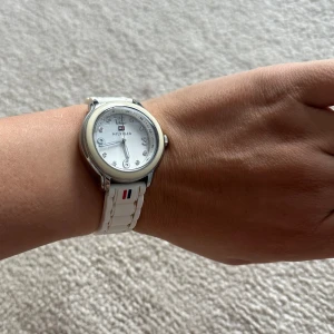 Vit klocka från Tommy Hilfiger - Säljer en stilren vit klocka från Tommy Hilfiger med silverfärgad boett och vit urtavla. Klockan har ett vitt armband i plast med Hilfigers logga och diskreta stenar som timmarkeringar. Perfekt accessoar för en fräsch look.