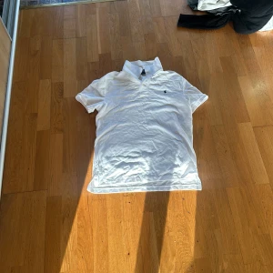 Vit pikétröja från Polo Ralph Lauren - Vit pikétröja från Polo Ralph Lauren i slim fit-modell. Klassisk krage med knappar och liten broderad logga på bröstet. Perfekt för en clean och stilren look.