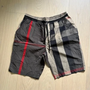 Badshorts med burberry mönster - Snygga shorts med svart, beige och röd rutig design. De har elastisk midja med snörning och sidofickor. Perfekta för sommardagar och har en modern, avslappnad look. Storleken Är 5XL men dom sitter som L/XL
