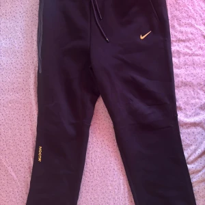Svarta mjukisbyxor från Nike NOCTA - Svarta mjukisbyxor från Nike NOCTA med gul logga på benet och liten gul Nike Swoosh på höften. Byxorna har dragsko i midjan och är tillverkade i mjukt material. Perfekta för en avslappnad stil. Passar bra för M också, pris kan diskuteras.