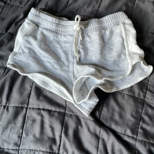 Ljusgrå mjukisshorts med snörning - Ljusgrå mjukisshorts från H&M med elastisk midja och vit snörning framtill. Shortsen har rundade kanter och är tillverkade i mjuk bomullsmix, perfekta för avslappnade dagar eller träning.