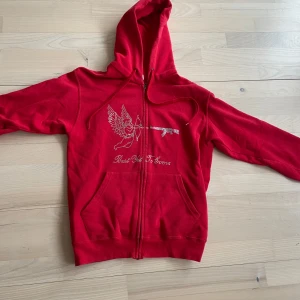 Röd hoodie med pärlor - Säljer en röd rhinestone hoodie med dragkedja och huva. På framsidan finns ett strasstryck med en ängel och texten 'Best Yet To Come'. Hoodien har fickor framtill och snören. Storlek S
