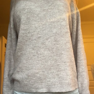 Ljusgrå stickad tröja - Mysig ljusgrå stickad tröja med rund hals och långa ärmar. Tröjan har en enkel och stilren design med ribbade muddar vid ärmslut och nederkant. Perfekt för lager-på-lager och passar till det mesta.