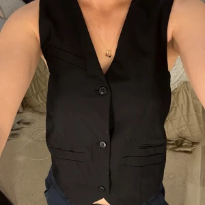 Svart kostymväst med knappar - Snygg svart väst med klassisk v-ringning och tre knappar framtill. Västen har två dekorativa fickor och är perfekt till sommaren.