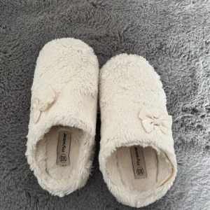Vita fluffiga tofflor  - Supermysiga vita tofflor från Mywear med fluffigt material och söt rosett på ovansidan. Ena tofflan har gått sönder i kanten, går säkert att sy ihop! Storlek 34/35