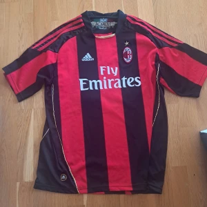 AC Milan retro fotbollströja  - Säljer en klassisk retro AC Milan matchtröja från Adidas med Gattuso 8 på ryggen. Tröjan är röd och svart med vita detaljer, kortärmad och har klubbmärke samt sponsortryck på bröstet. Perfekt för fans av italiensk fotboll.