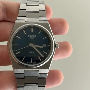 Tisso PRX herrklocka i stål med blå urtavla - Snygg Tisso PRX herrklocka med blå urtavla och datumvisning. Klockan har ett stilrent armband i borstat stål och silverfärgad boett. Perfekt accessoar för dig som gillar klassisk och modern design.