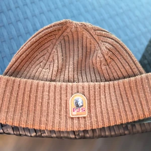 Brun ribbad mössa från Parajumpers - Säljer en brun ribbstickad mössa från Parajumpers med uppvikt kant och två tydliga logotyper framtill. Perfekt accessoar för kyliga dagar. 9/10 använd 1 gång nypris 700 perfekt för kalla sommarkvällar