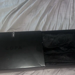 Svarta fotbollsskor Adidas Copa - Säljer ett par svarta Adidas Copa fotbollsskor med klassisk design. Skorna har skruvdobbar och är tillverkade i syntetmaterial med en stilren look utan snörning. Perfekta för matcher på gräsplan. Helt nya och elite skor  