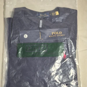 Mörkblå t-shirt från Polo Ralph Lauren - Säljer en mörkblå t-shirt från Polo Ralph Lauren med klassisk röd broderad logga. Om du ser en till liknande annons är för att jag köpte två T-shirts till mig själv, men i fel storlek. Därmed är den helt ny, oanvänd, och bara öppnad för bilder