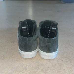 Gröna sneakers från Axel Arigato i mocka - Säljer ett par gröna sneakers från Axel Arigato i mjuk mocka med vita sulor. Skorna har snörning och diskret logga i guld på sidan. Perfekta för dig som gillar stilrena och trendiga skor. Priset kan diskuteras.