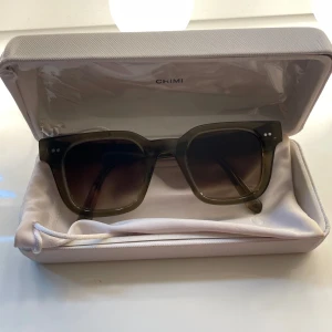 Olivgröna solglasögon från CHIMI - Snygga solglasögon från CHIMI i en olivgrön transparent färg med fyrkantig form och mörka glas, size 04. Kommer med originalfodral och tygpåse. Perfekta för att ha nu till sommarn. Ungefär 1 år gamla och inga defekter, förutom att bågarna är lite uttöjda men inget som ej går att fixa. 💕 skriv för fler bilder/frågor. Pris kan diskuteras vid snabb affär💕 tar även emot byte av 08