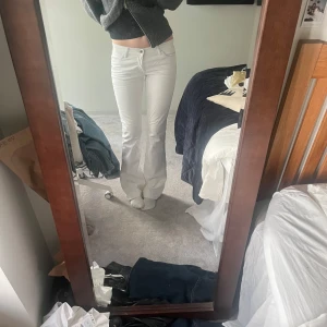 Vita bootcut jeans - Säljer ett par vita bootcut jeans med låg midja och klassisk femficksdesign. Byxorna har en snygg passform som sitter tajt upptill och släpper ut vid benen. Perfekta för en stilren och fräsch look.