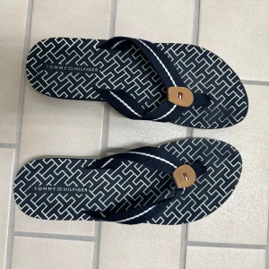 Mönstrade flip-flops från Tommy Hilfiger - Snygga flip-flops från Tommy Hilfiger med marinblå och vita mönster på sulan samt tygremmar med läderdetalj och logga. Använda två gånger 🫶🏻