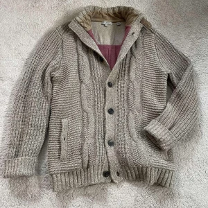 Ted baker stickad kofta: M - Säljer en snygg beige stickad kofta från Ted Baker med knappar framtill. Koftan har en ribbad krage och muddar, samt ett mönster av flätor och ränder. Perfekt för kyliga dagar! Hör av dig om du har fler frågor eller funderingar 🤩🥂