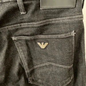 Svarta jeans från Emporio Armani - Snygga svarta jeans från Emporio Armani med klassisk femficksdesign och silverfärgad logga på bakfickan. Jeansen har raka ben och normal passform, perfekta till många olika stilar.