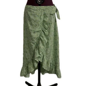 Grön blommig omlottkjol med volang - Säljer en grön lång omlottkjol med småblommigt mönster och volangkant nertill. Kjolen knyts i med en rosett och har en luftig och flowy känsla. Perfekt för dig som gillar romantiska vibes och vill ha något extra till sommaren. Endast använd en gång!