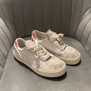 Vita sneakers från Inuiiki med rosa detaljer, PRIS KAN DISKUTERAS - Säljer ett par vita sneakers från Inuiiki med bred sula och rosa textdetalj på hälen. Skorna har snörning. DEM SKA SE SLITNA UT. Jag har inte använt dem mycket alls men min hund har bitit lite på dem. 