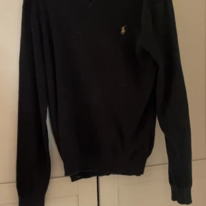 Svart v-ringad tröja från Ralph Lauren - Klassisk svart v-ringad tröja från Ralph Lauren med den ikoniska broderade loggan på bröstet. Tröjan har långa ärmar och är tillverkad i mjukt material som passar perfekt till många olika outfits. Ge pris förslag med 