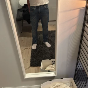 Blå jeans från J.Lindeberg - Säljer ett par klassiska blå jeans från J.Lindeberg med normal passform och raka ben. Jeansen har fem fickor, gylf med dragkedja och knapp samt läderpatch med logga bak i midjan. Perfekta till vardags och enkla att matcha.