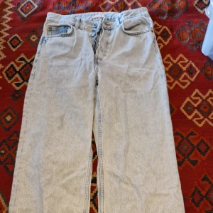 Ljusblå jeans med råa kanter från H&M - Ljusblå jeans från H&M i rak modell med hög midja och råa, fransiga benslut. Klassisk femficksdesign och dragkedja med knapp. Perfekta för en avslappnad och trendig look.