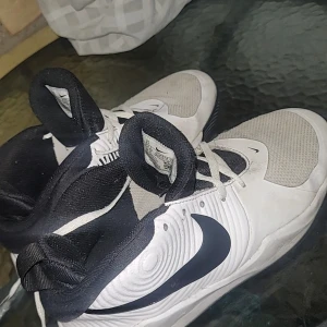 Vita och svarta Nike sneakers - Nike sneakers i vitt och svart med gröna innersulor. Skorna har en sportig design med mesh framtill, snörning och tydlig svart swoosh på sidorna. Ovandelen är i syntet och textil, perfekt för dig som gillar en clean och modern look.