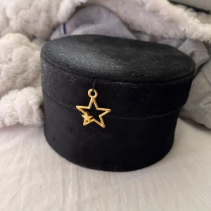 smyckeskrin - Superfin rund smyckesväska i svart sammet med en guldig stjärnberlock framtill. Insidan är ljusbeige med spegel i locket och flera fack för ringar och smycken. Perfekt att ha på resan eller hemma på hyllan.