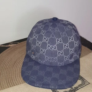 Dubai blue Gucci Keps - Snygg blå keps från Gucci med ikoniskt GG-mönster över hela kepsen. Justerbar rem bak och diskret guldfärgad GG-detalj på sidan. Tillverkad i tålig bomull med klassisk böjd skärm. Perfekt för dig som vill sticka ut med en lyxig streetstyle. Säljer denna pågrund av att den är för stor. Men är helt ny! Öppen för byten!!