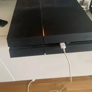 Playstation4 - Ingen bok syns på bilden, endast en spelkonsol (PlayStation 4) med en USB-kabel ansluten. Ingen information om boktitel, författare eller innehåll kan extraheras från denna bild.