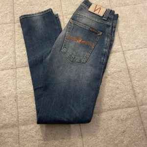Blå jeans från Nudie Jeans - Snygga blå jeans från Nudie Jeans med klassisk femficksdesign och coola kontrastsömmar på bakfickan. Jeansen har en rak passform och är tillverkade i slitstarkt denim. Perfekta för dig som gillar en tidlös och avslappnad stil.