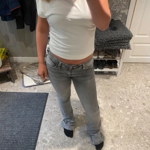 Grå bootcut jeans med kontrastsömmar - Säljer ett par grå jeans med bootcut-modell och snygga kontrastsömmar på bakfickorna. Jeansen har låg midja. Jeansen har täcken på slitage, kolla sista bilderna. Köpare betalar frakt!