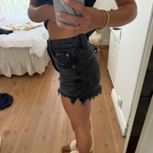 Svarta jeansshorts med fransad kant - Snygga svarta jeansshorts med hög midja och rå fransad kant. Klassisk femficksmodell med knappar framtill. Perfekta för sommarens alla äventyr och har en cool, lite sliten look som passar till allt.